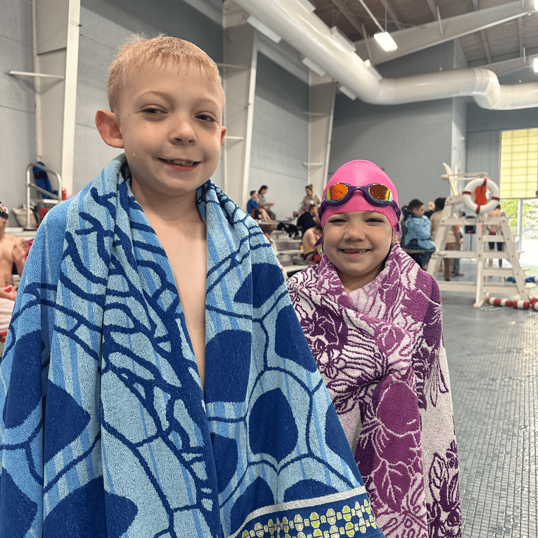 Two participants standing poolside after a swim, covering themselves with towels.