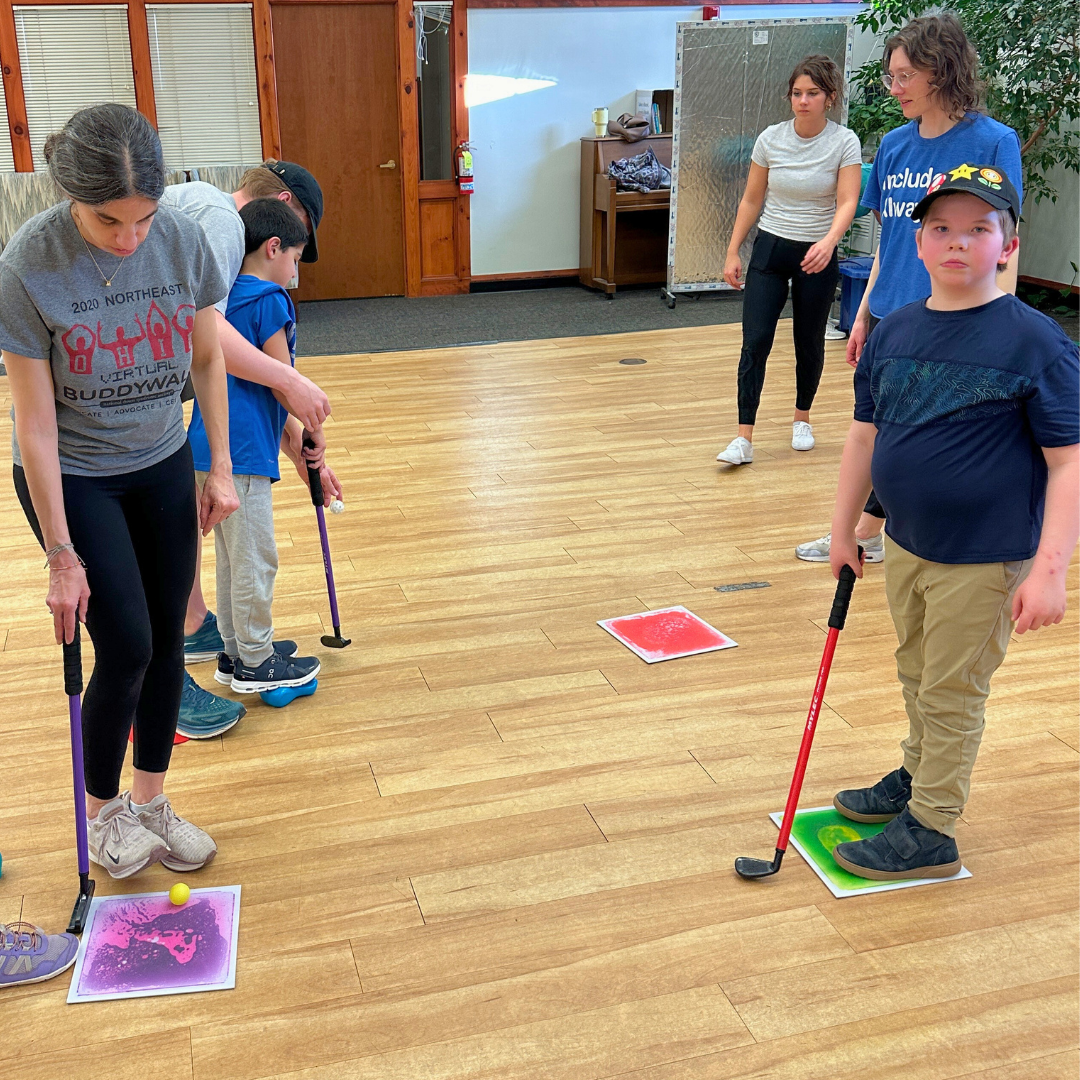 A small group of young participants, guided by a therapist, are engaged in a session where they are instructed to place ping pong balls on colored squares on the floor using putters..